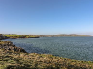 A coastal landscape with grassy cliffs and a large body of water under a clear blue sky at Haulfryn in Moelfre