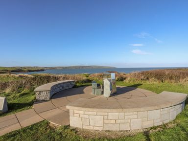 A stone circular seating area with metal sculptures overlooking a coastal view at Haulfryn in Moelfre