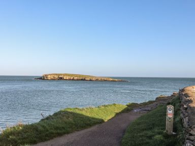 A coastal path next to the sea with an island in the distance at Haulfryn in Moelfre