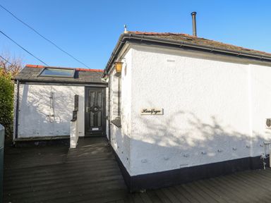 The exterior of a white building with a black door a wooden deck and a sign that says Haulfryn at Haulfryn in Moelfre