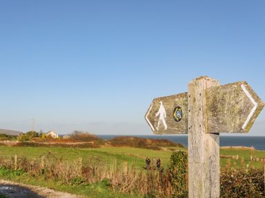 A wooden walking trail signpost in a grassy field with a view of the ocean and people walking at Haulfryn in Moelfre