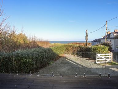 A gravel driveway with bushes on both sides a white gate and houses on the right near the sea at Haulfryn in Moelfre