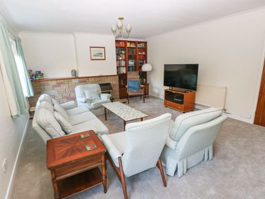 A living room with a sofa set a coffee table a wooden side table a television on a stand a bookshelf and an armchair at 30 Long Shepherds Drive Newton near The Mumbles