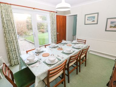 A dining room with a table set for six people near glass doors showing a garden at 30 Long Shepherds Drive Newton near The Mumbles