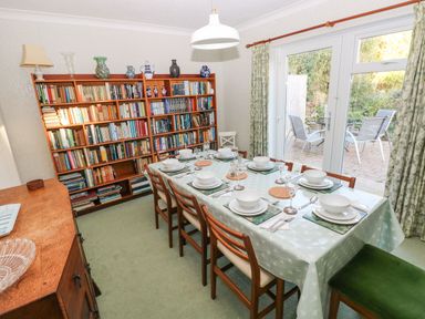 A dining room with a set table and a bookshelf next to glass doors leading outside at 30 Long Shepherds Drive Newton near The Mumbles