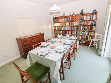 A dining room with a set table with bowls and glasses next to a wooden bookshelf filled with books at 30 Long Shepherds Drive in Newton near The Mumbles