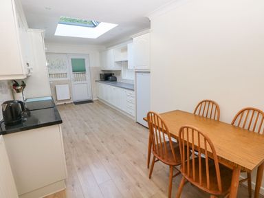 A kitchen with white cabinets a skylight wooden floor a dining table with four chairs and kitchen appliances at 30 Long Shepherds Drive Newton near The Mumbles