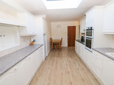 A kitchen with white cabinets wooden floor a dining table with chairs and built in ovens at 30 Long Shepherds Drive in Newton near The Mumbles