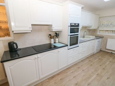 A kitchen with white cabinets black countertop built in ovens sink dishwasher and wooden floor at 30 Long Shepherds Drive Newton near The Mumbles
