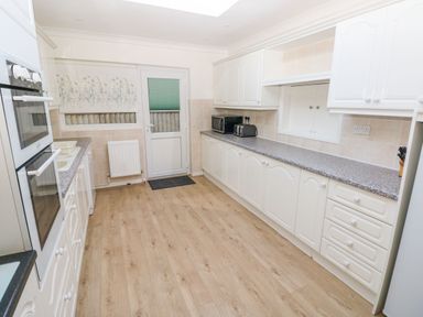 A kitchen with white cabinets, countertop appliances, an oven, sink, and wooden floor at 30 Long Shepherds Drive in Newton near The Mumbles