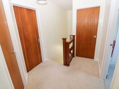A hallway with three wooden doors and carpeted floor at 30 Long Shepherds Drive in Newton near The Mumbles