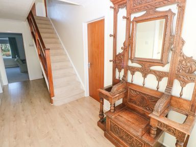 A hallway with wooden flooring a carpeted staircase a closed wooden door and an ornate wooden hall stand with a mirror at 30 Long Shepherds Drive Newton near The Mumbles
