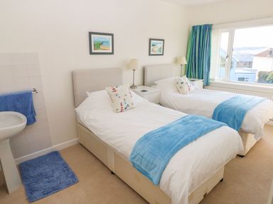 A bedroom with two single beds bedside tables lamps and a sink by the window at 30 Long Shepherds Drive in Newton near The Mumbles