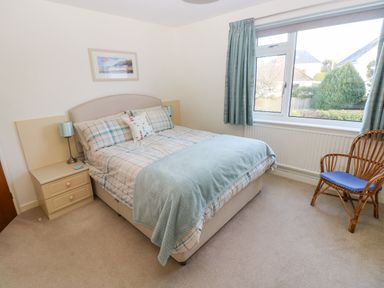 A bedroom with a double bed bedside tables a rattan chair and a window with curtains at 30 Long Shepherds Drive in Newton near The Mumbles