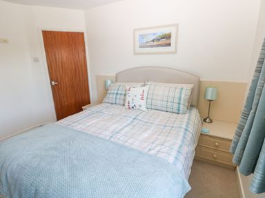 A bedroom with a bed covered in plaid bedding beside a wooden door at 30 Long Shepherds Drive in Newton near The Mumbles