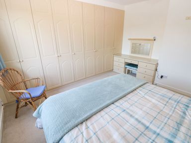 A bedroom with a bed with a plaid duvet and blue blanket a rattan chair and built in wardrobes at 30 Long Shepherds Drive in Newton near The Mumbles