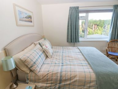 A bedroom with a bed pillows bedside lamp window with curtains and a wicker chair at 30 Long Shepherds Drive Newton near The Mumbles