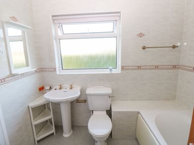 A bathroom with a pedestal sink toilet corner shelves and a bathtub at 30 Long Shepherds Drive in Newton near The Mumbles