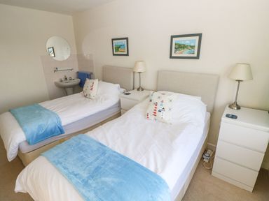 A bedroom with two single beds blue blankets and decorative pillows with a white sink and round mirror at 30 Long Shepherds Drive Newton near The Mumbles