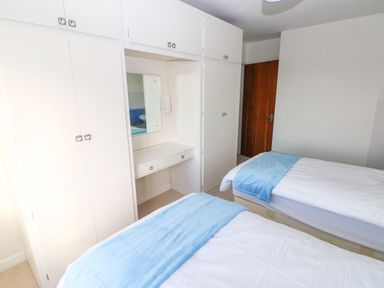 A bedroom with two single beds white wardrobes and a dressing table at 30 Long Shepherds Drive in Newton near The Mumbles