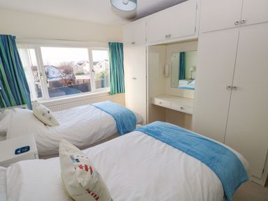 A bedroom with two single beds white built in wardrobes and a window with blue curtains at 30 Long Shepherds Drive in Newton near The Mumbles