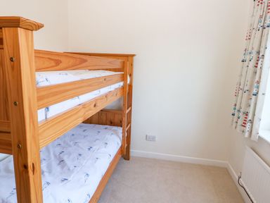 A bedroom with a wooden bunk bed and patterned curtains at 30 Long Shepherds Drive in Newton near The Mumbles