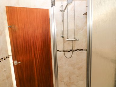 A bathroom with a wooden door and a tiled shower area with a showerhead at 30 Long Shepherds Drive in Newton near The Mumbles