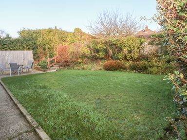 A backyard with grass lawn shrubs and a patio table with chairs at 30 Long Shepherds Drive in Newton near The Mumbles