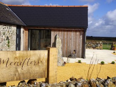 A farmhouse exterior with stone and wooden walls a wooden sign reading Menifters and a garden area at The Rum House in Porthallow