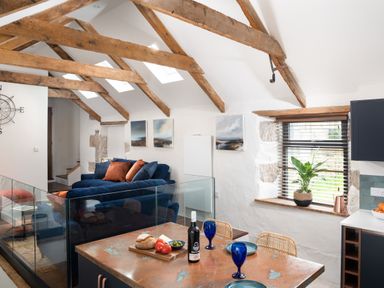 A kitchen and living area with wooden beams glass railing blue sofa and dining table at The Rum House in Porthallow