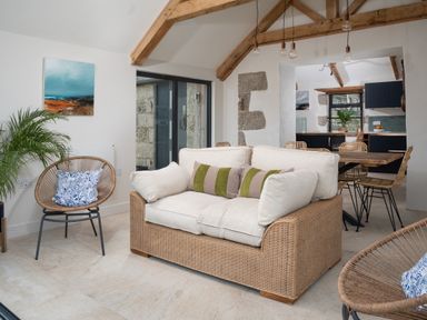 A living room with a wicker sofa, woven chairs, a wooden dining table, and exposed ceiling beams at The Rum House in Porthallow