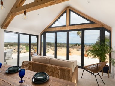 A dining and sitting area with large windows showing an outdoor patio at The Rum House in Porthallow