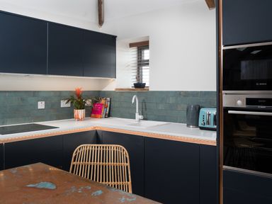 A kitchen with dark cabinets a white countertop a sink a toaster a kettle and a wicker chair at The Rum House in Porthallow