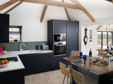 A kitchen with dark cabinets wooden beams and a dining table with wicker chairs at The Rum House in Porthallow