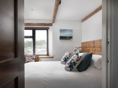 A bedroom with a wooden bedframe white bedding and decorative pillows near a window with blinds at The Rum House in Porthallow