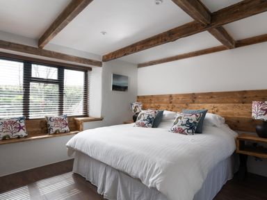 A bedroom with a large bed wooden headboard wooden ceiling beams window with blinds and decorative pillows at The Rum House in Porthallow