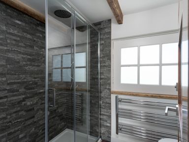 A bathroom with a glass enclosed shower area a chrome towel rack and a window at The Rum House in Porthallow