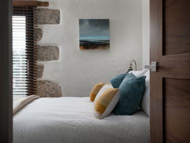 A bedroom with a bed with pillows next to a window with wooden blinds and a painting on the wall at The Rum House in Porthallow