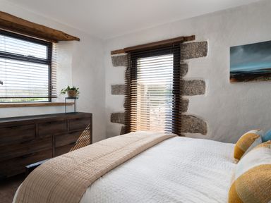 A bedroom with a bed a wooden dresser and windows with blinds at The Rum House in Porthallow