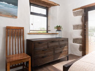 A room corner with a wooden chair and a wooden dresser with a plant on top at The Rum House in Porthallow