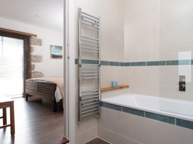 A bathroom with a bathtub and towel rack next to a bedroom with a wooden bed at The Rum House in Porthallow