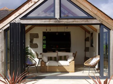 A living area with a sofa and chairs inside a house with large glass doors at The Rum House in Porthallow