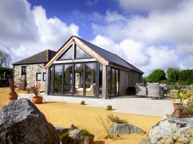 Stone cottage with glass front and outdoor seating area with potted plants at The Rum House in Porthallow