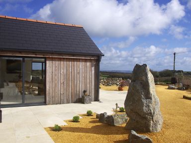An outdoor area with gravel, large rocks, small plants and a wooden building with a glass door at The Rum House in Porthallow