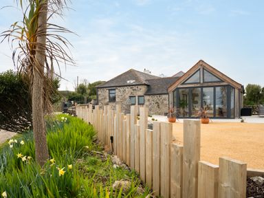 A stone house with large glass windows and a wooden fence with plants in front at The Rum House in Porthallow