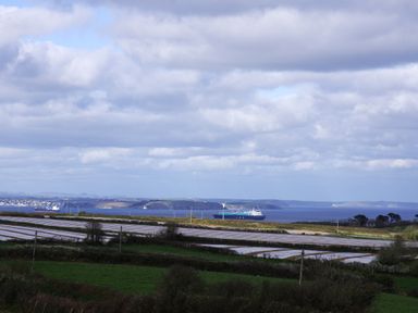 A coastal landscape with fields in the foreground and cargo ships on the water at The Rum House in Porthallow