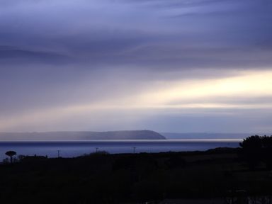 A coastal landscape with a body of water and distant hills under a cloudy sky