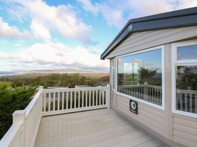 A deck with white railing outside a mobile home with windows showing countryside and hills at Gwent 74 in Borth