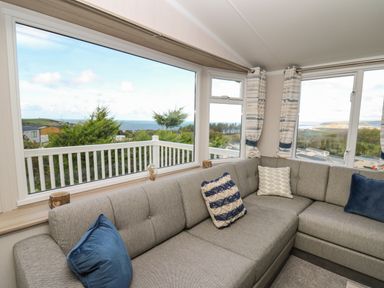 A living room with a gray sectional sofa and blue and white cushions by large windows overlooking greenery and a seaside view at Gwent 74 in Borth