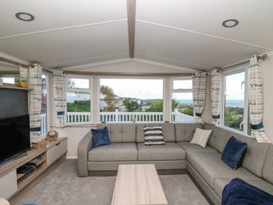 A living room with a gray sectional sofa blue and patterned cushions a wooden coffee table and a TV unit with a television at Gwent 74 in Borth